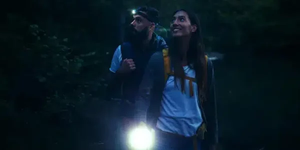 Close up photo of two hikers walking with flashlight at night in the woods.