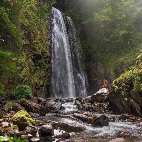 A tourist standing next to a Monteverde Waterfall.