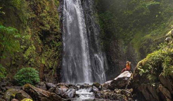 A tourist standing next to a Monteverde Waterfall.