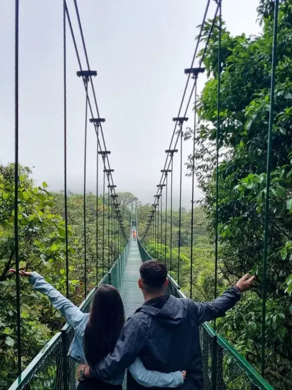 A couple on a suspended bridge in Monteverde, giving you the welcome to Monteverde Tours.